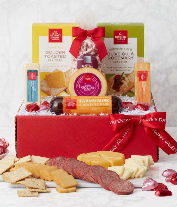 A red gift box with a red "Happy Valentine's Day" Ribbon. Inside are blocks of cheddar, gouda, and jack cheeses, summer sausage, pretzels, and boxes of golden toasted and Olive Oil & Rosemary Crackers