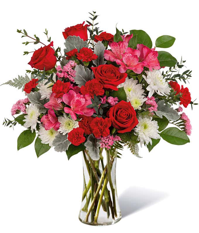 Flowers of red, pink, and white arranged into a tall red sparkly vase.