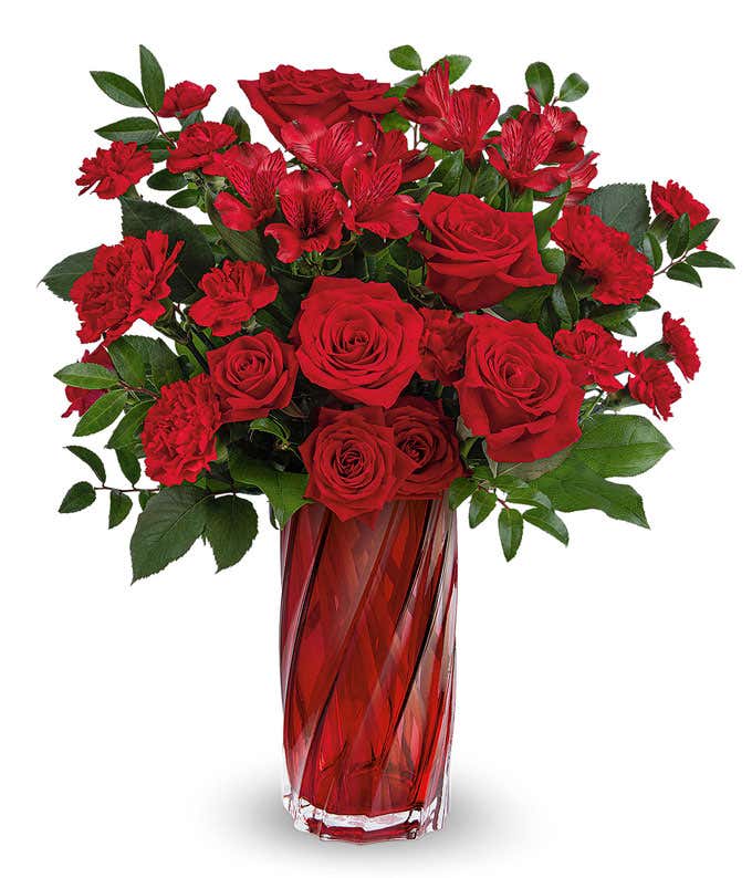 A bouquet with red roses, alstroemeria, and carnations with floral greens in a red glass vase 