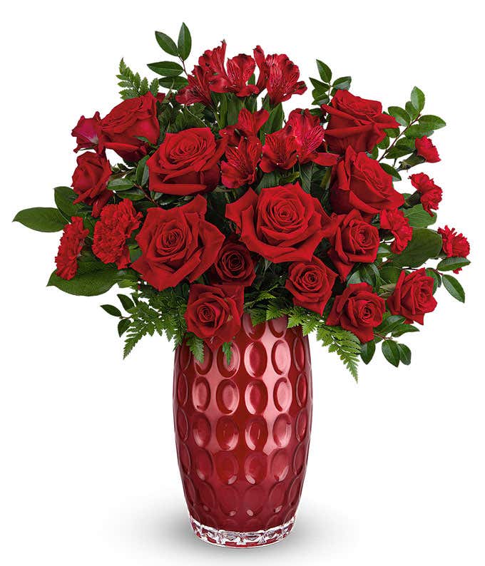 Red roses and red spray roses with floral greens in a tall red cylinder glass vase