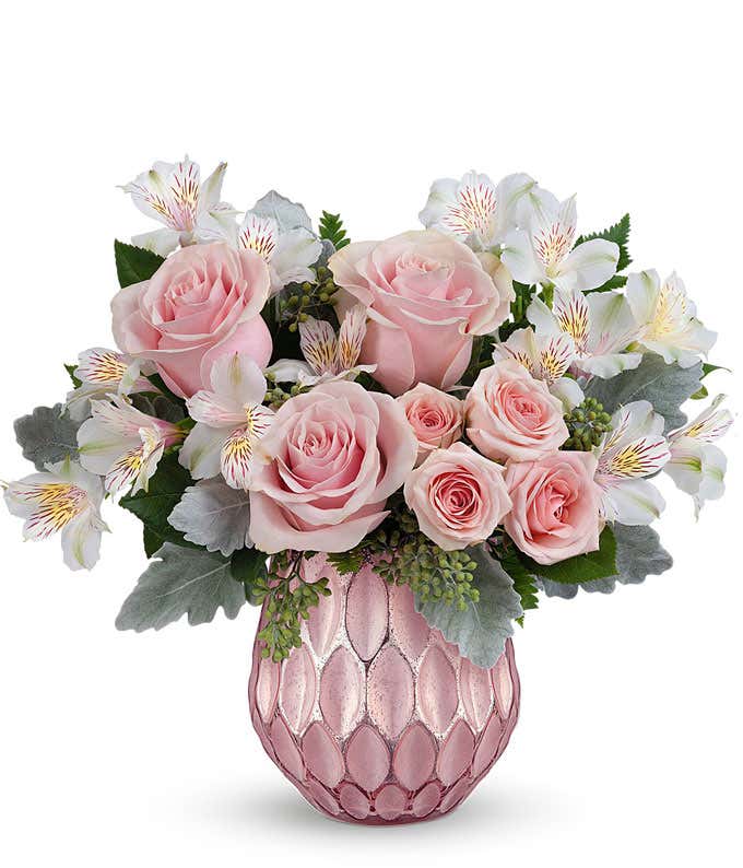 A bouquet of light pink roses, light pink roses, & white alstroemeria with floral greens in a metallic pink vase with geometric textures