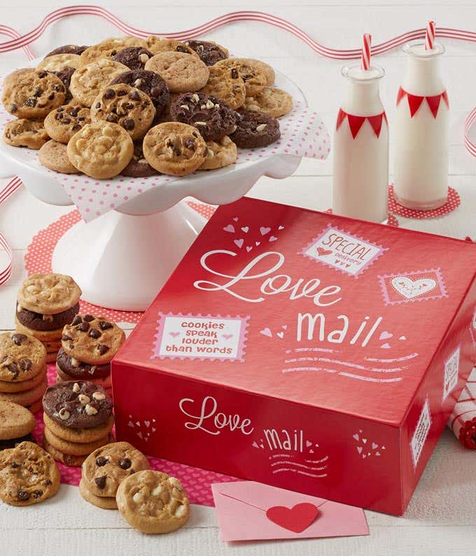 A red gift box with stamp illustrations that says "Love Mail" on two sides. An assortment of included cookie flavors laid out and on a white serving tray. 
