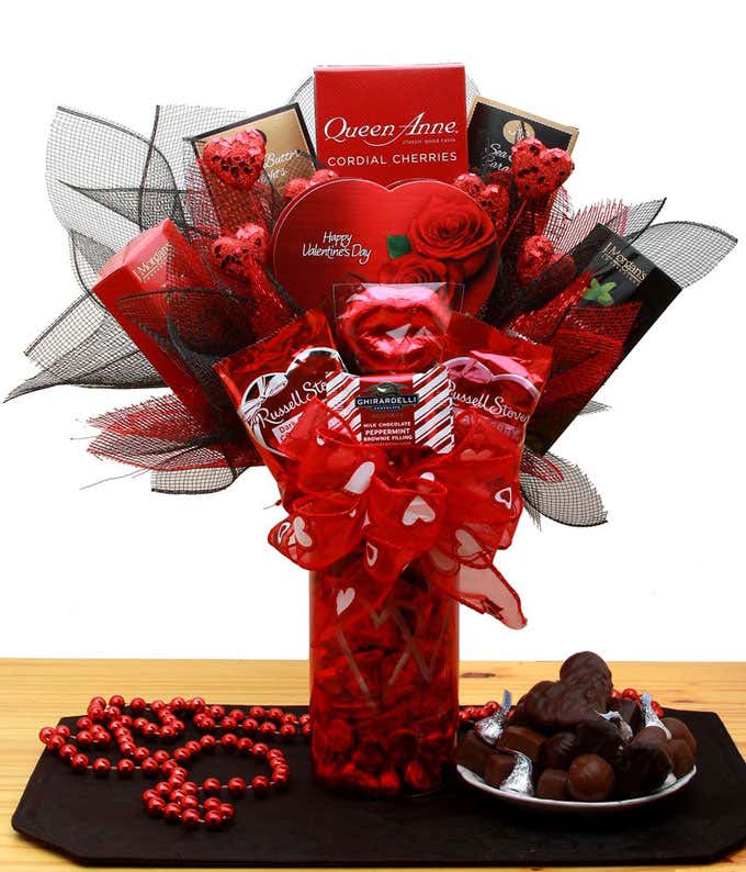 A gift bouquet in a red vase with red ribbon. Items splayed out like a bouquet with red and black ribbon 