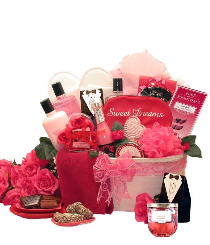 A white gift tin with pink ribbon. Pink scented candles, a pink loofah, body gel, body lotion, pink sleep mask, and more included items can be seen 