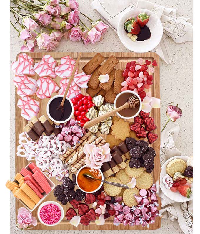 A charcuterie board laid out with biscoff cookies, wafer cookies, chocolate kisses, honey, and chocolate sauce. Other items include chocolate dipped pretzels and other chocolates.
